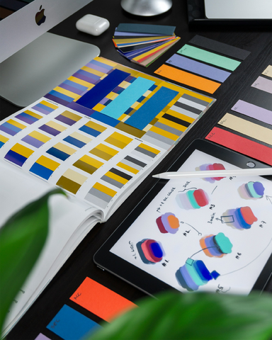 multiple paper samples of colour on a desk with a mac computer in the background